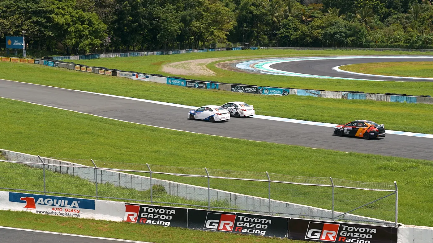Wide circuit view with race cars approaching through a corner